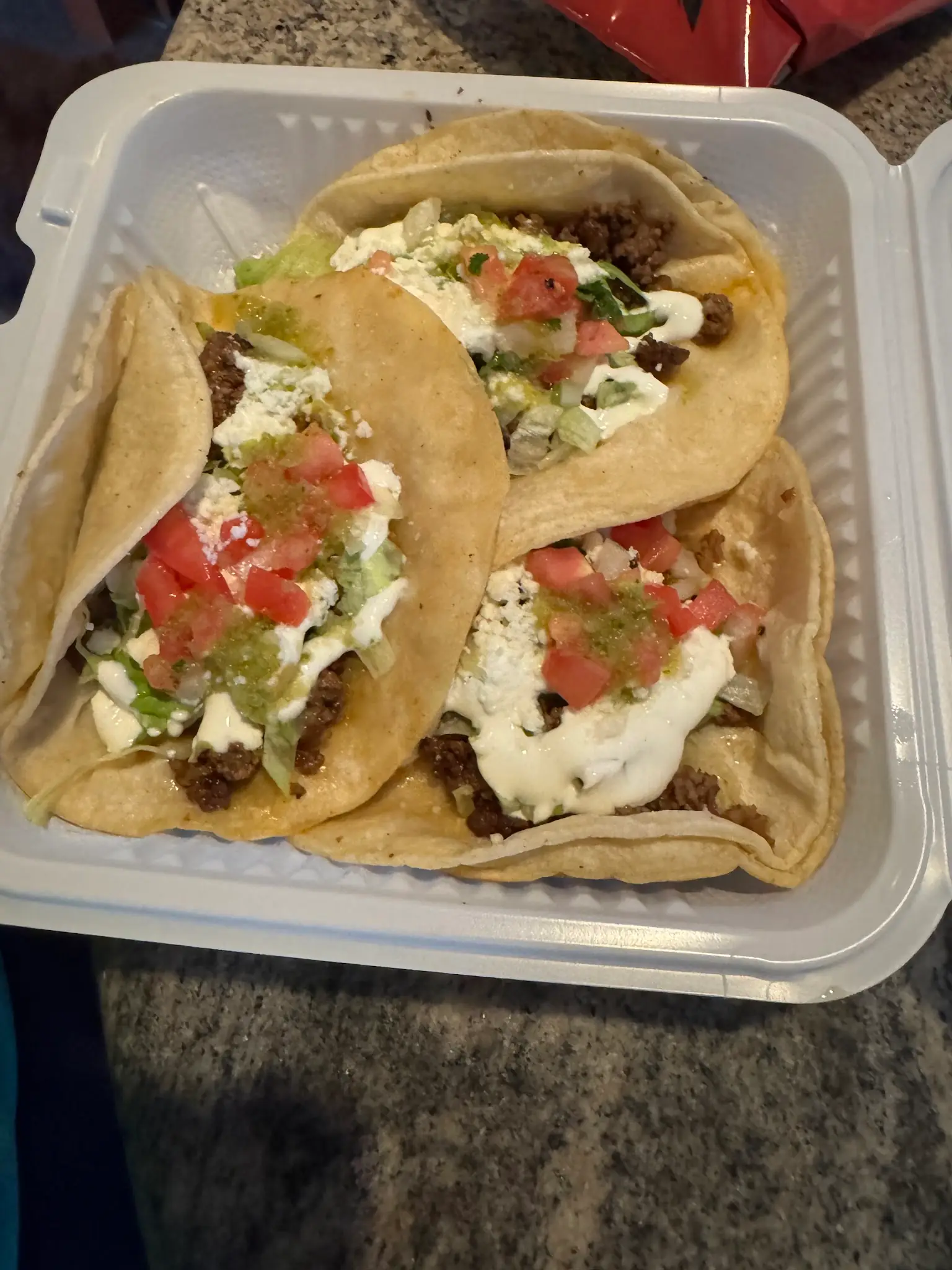 Three beef tacos with crema and diced tomato in a takeout box