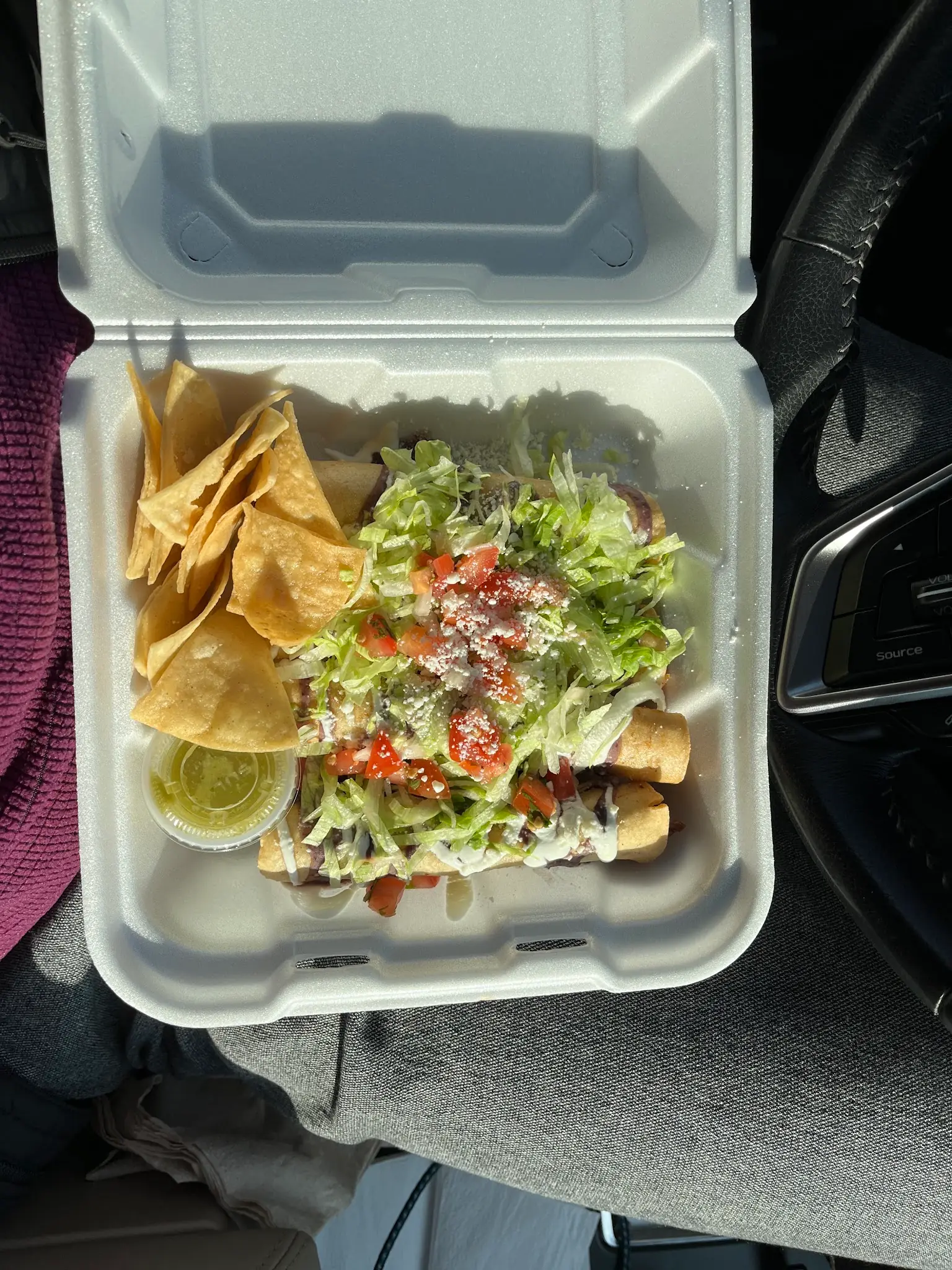 Tacos dorados under lettuce, crema, crumbled cheese and diced tomato, with tortilla chips, in a takeout box